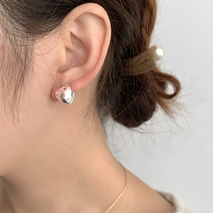 Close-up of heart-shaped silver stud earrings with pink bow detail on a model