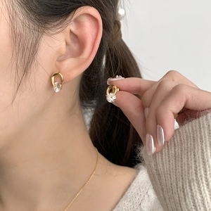 Close-up of minimalist gold interlocking earrings with zircon on a model's ear