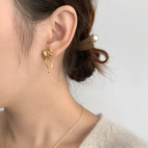 Élégantes boucles d'oreilles nœud doré au design de ruban fluide sur mannequin pour un look