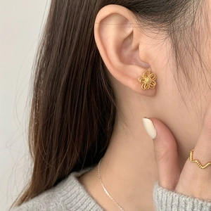 Detailed view of hollow floral gold stud earrings with delicate woven texture on model