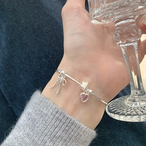 Detail of silver bangle with pink heart gemstone, star and bow charms on wrist