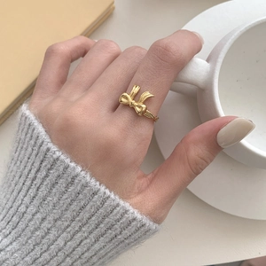 Close-up of golden bow ring on finger styled with a cozy knit sweater and a coffee cup
