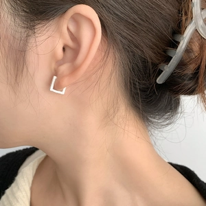 Gros plan de boucles d'oreilles carrées en argent mat portées par un mannequin de style épuré