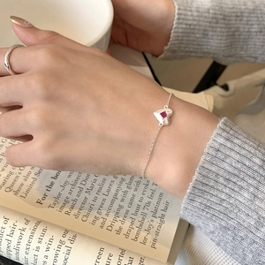 Detail of silver heart bracelet with pink gemstone on woman wearing grey sweater