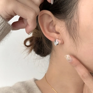Detailed close-up of a silver heart stud earring with pink bow worn by a model