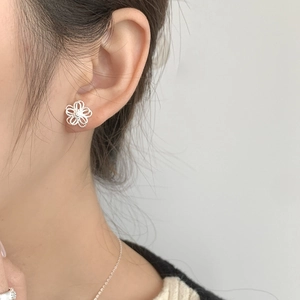 Detail view of dainty 925 sterling silver hollow flower stud earrings on a female model