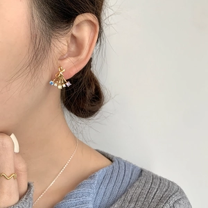 Macro view of fan-shaped gold earrings with colorful zircons and bow details on a model