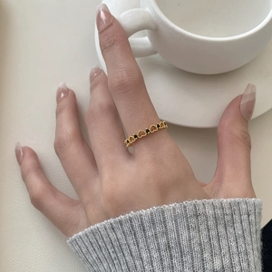 Detail of a gold heart-shaped ring with black stones worn in a minimalist lifestyle setting