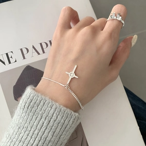 Silver S925 star cross bracelet and bow ring shown on model against a magazine