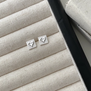 Macro view of square silver heart earrings with textured grid base on a beige display