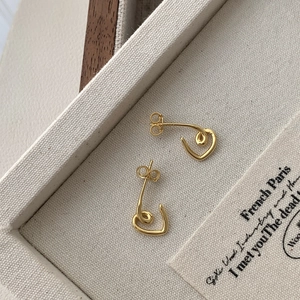 Detailed view of minimalist gold heart stud earrings on a beige textured jewelry tray