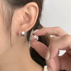 Detail shot of silver S925 earrings featuring pink bow patterns on polished metal spheres