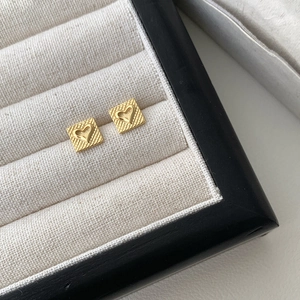 Close-up of golden S925 sterling silver heart studs with grid texture in a jewelry box