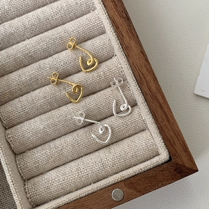 Close-up of minimalist gold and silver heart outline stud earrings in velvet box