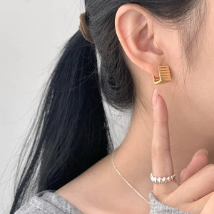 Detail of gold geometric hollow square earrings worn with silver rings and a chain necklace