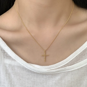 Gros plan d'un collier croix doré au design perlé porté par un mannequin sur blanc