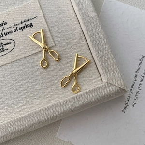 Macro shot of gold-plated scissor shaped silver earrings on a minimalist cream fabric display