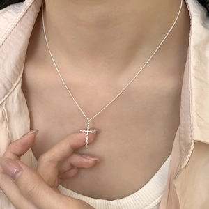 Détail du pendentif croix à perles sur chaîne argentée porté avec une tenue sobre