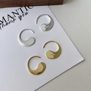 Close-up of S925 hallmark on curved silver and gold teardrop earrings on a white card