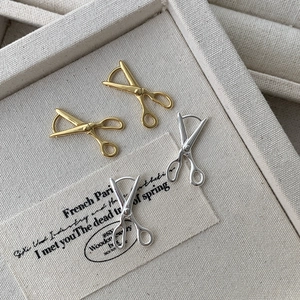 Detail shot of silver and gold scissors shaped hoop earrings on a beige jewelry display
