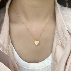 Close-up of golden heart pendant necklace with frosted texture worn on a model