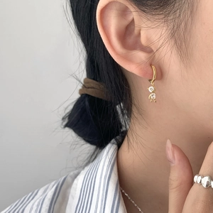 Minimalist gold hoop earrings featuring two clear dangling zircon stones on female model
