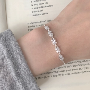 Macro shot of silver rectangular zircon bracelet worn over a grey knit sweater