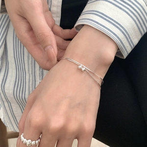 Close-up of double-layer silver bracelet with ball charms and textured wave ring on hand