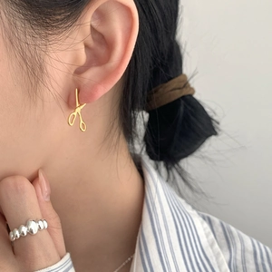 Detail of creative gold-plated scissors earrings and beaded silver ring on a model