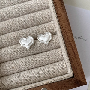 Close-up of heart-shaped silver earrings with brushed matte finish in a jewelry box