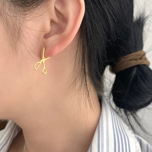 Close-up of gold scissors-shaped S925 sterling silver hoop earring worn on an ear