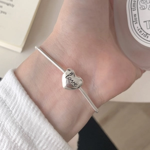 Macro shot of silver heart charm with Love engraving on a sleek snake chain bracelet