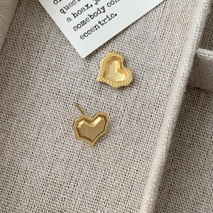 Minimalist geometric heart earrings with brushed gold finish on beige linen tray