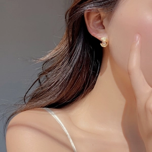 Détail d'une boucle d'oreille spirale dorée avec perle blanche sur l'oreille d'un modèle