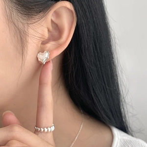 Close-up of heart-shaped brushed silver stud earrings and beaded ring on model
