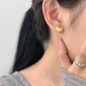 Macro view of golden heart stud earrings with brushed texture on model's ear