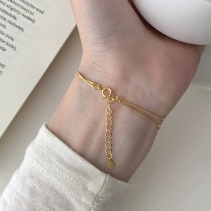 Detail of a layered gold snake chain bracelet with water drop pendant and lobster clasp