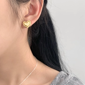 Close-up of golden heart earrings with brushed texture on model in minimalist style