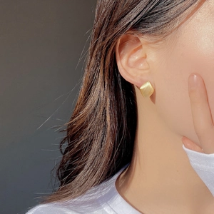 Detail of matte brushed gold geometric square earrings worn by a model in natural light