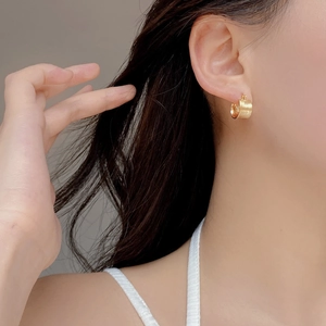 Dettaglio di orecchini a cerchio in oro spazzolato indossati per un look moderno