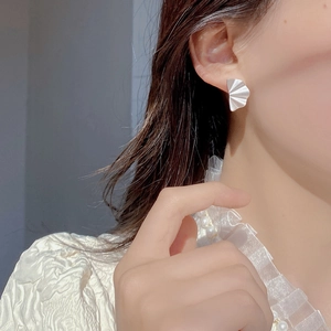 Macro detail of silver fan-shaped pleated stud earring with matte metallic texture