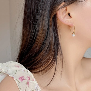Elegant gold hook earrings with natural white pearls on a model for a minimalist look