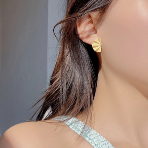 Macro detail of gold fan-shaped earring with radiant pleated texture on earlobe