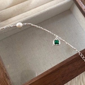 Macro detail of silver bead bracelet featuring a green zircon charm and white pearl
