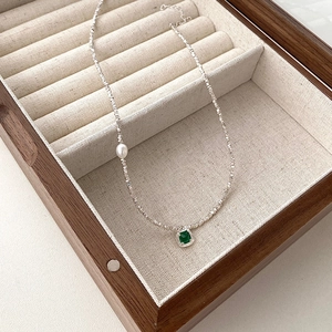 Macro detail of S925 silver necklace featuring an emerald zircon and a small pearl