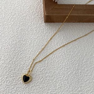 Close-up of golden beaded chain necklace with heart pendant featuring black onyx inlay
