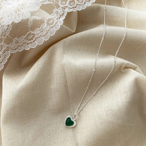 Detail of S925 silver chain necklace featuring green heart pendant on beige linen