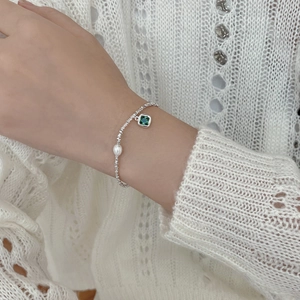 Detail of silver beaded bracelet with single pearl and emerald pendant on model