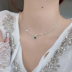 Close-up of S925 silver necklace with emerald zircon and pearl on a lace outfit