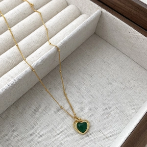 Close-up of a gold heart necklace with green agate inlay on a cream fabric jewelry box